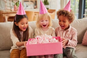 Colorful birthday celebration with kids opening a gift box of pink tissue paper.