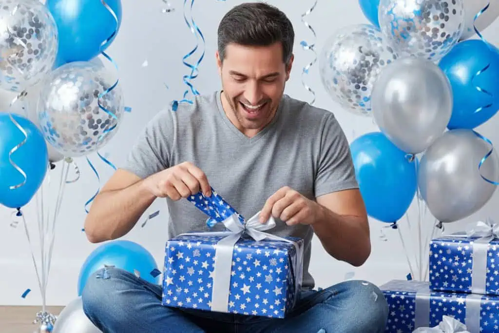 Vibrant man opening a gift surrounded by blue and silver balloons for special occasion celebration.